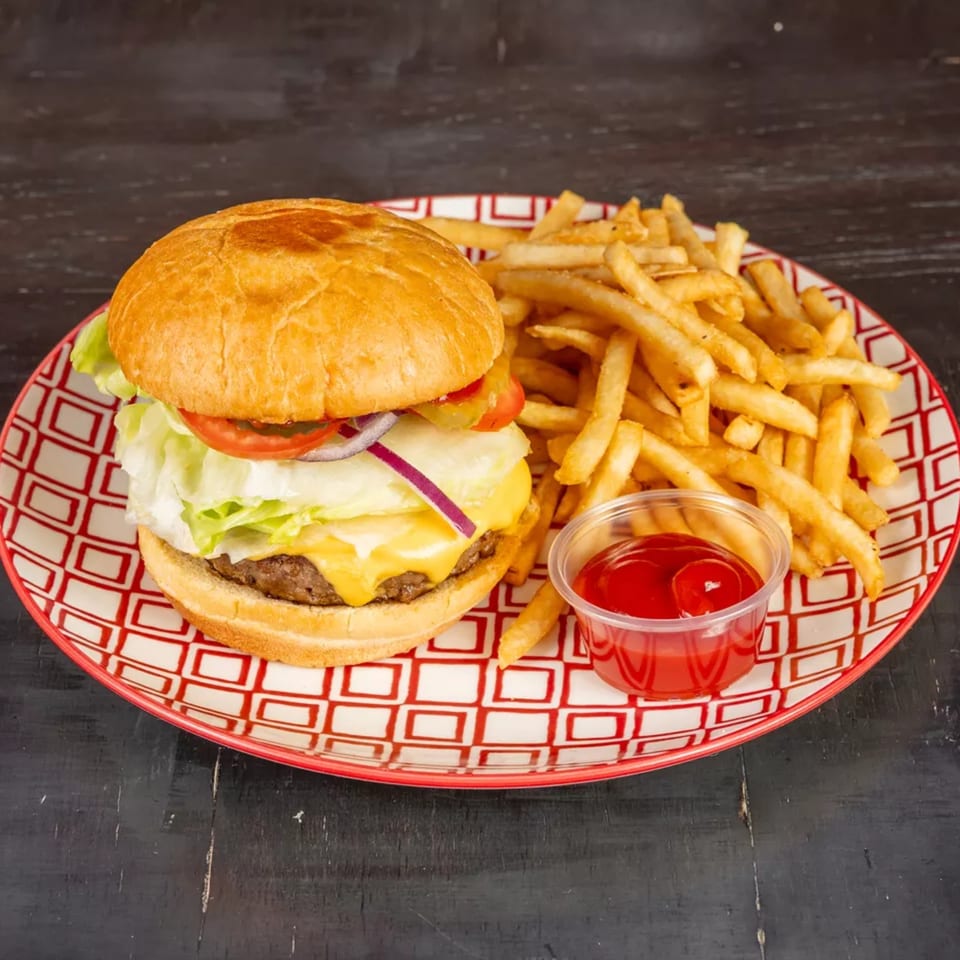 Cheeseburger with lettuce, tomato, onion, and pickles, served with fries and ketchup on a red and white plate.