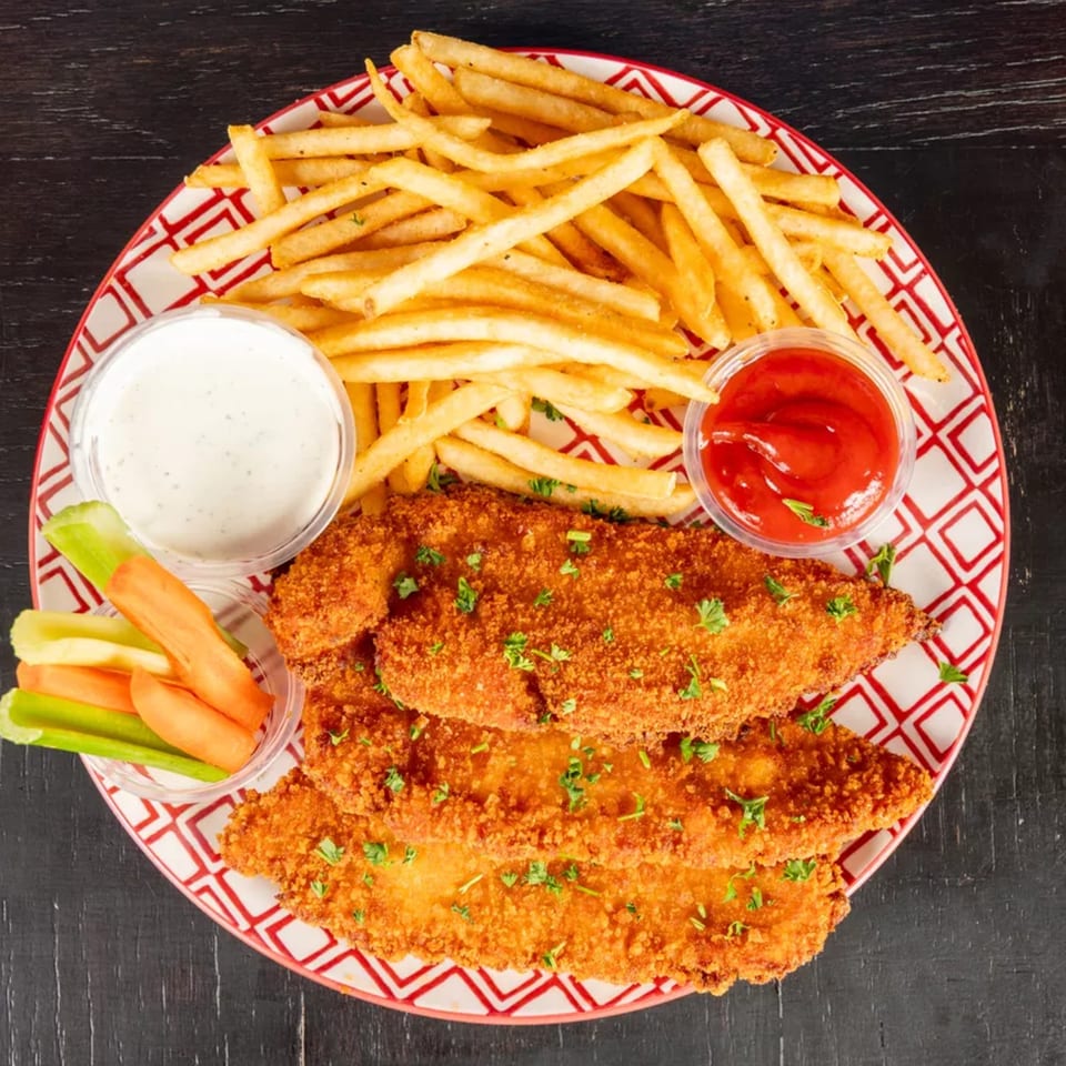 Crispy chicken tenders, golden french fries, ranch, ketchup, and vegetable sticks on a red and white plate.