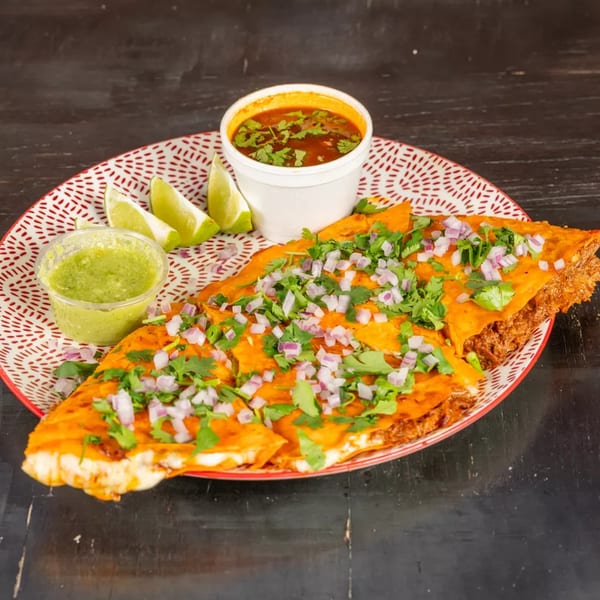 Birria quesadillas topped with cilantro and red onions, with consome, salsa verde, and lime wedges.