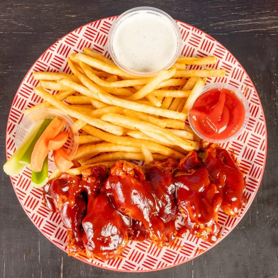 A plate of BBQ chicken wings, golden fries, celery, carrots, ranch, and ketchup.