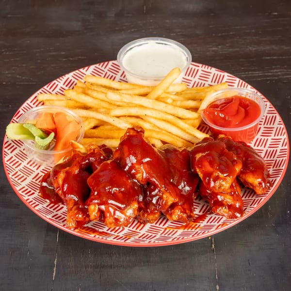 A plate of barbecue chicken wings with french fries, ranch, ketchup, and pickled vegetables.