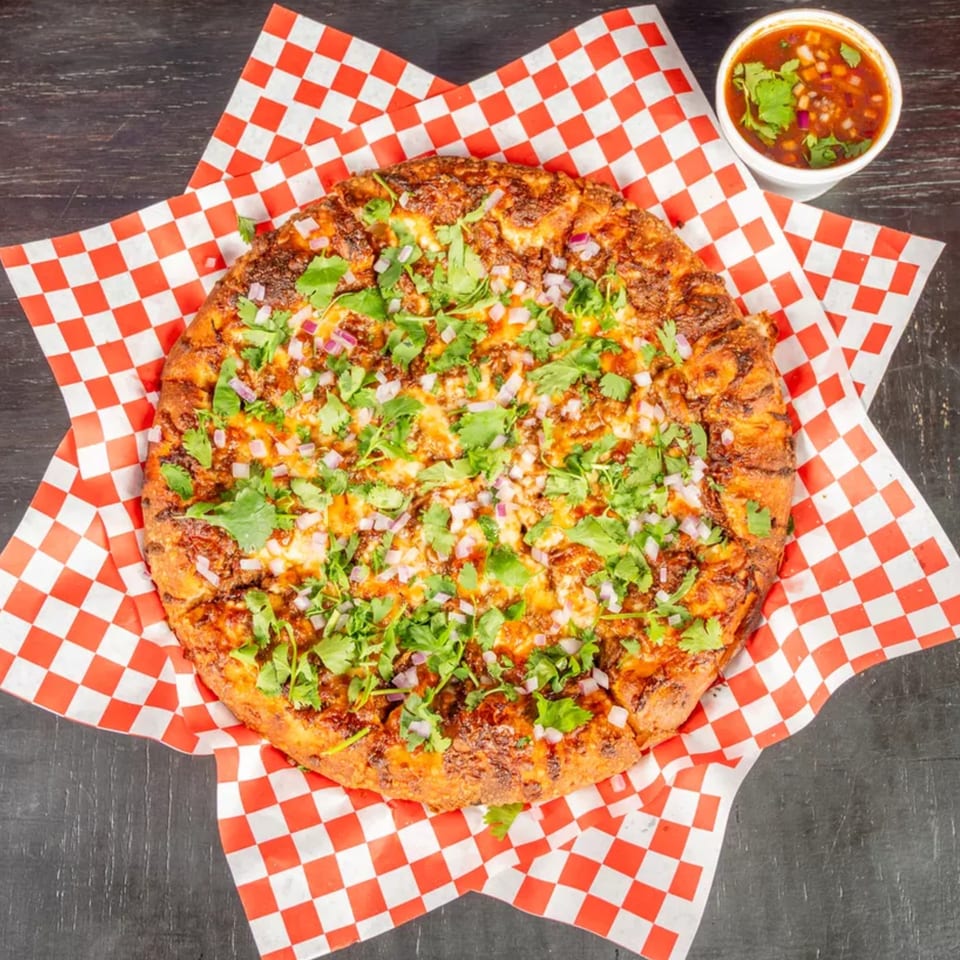 A round, cheesy pizza topped with cilantro and red onions, served on red and white checkered paper.