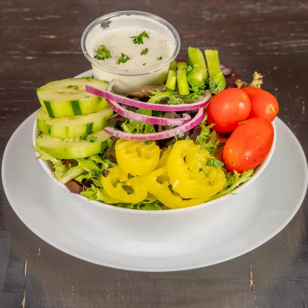 A fresh garden salad with cucumbers, red onions, tomatoes, and banana peppers, with a side of ranch dressing.
